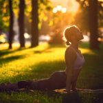 Eine Person praktiziert eine Yoga-Pose im Freien auf einer grasbewachsenen Fläche während des Sonnenuntergangs.