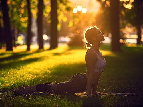 Eine Person praktiziert eine Yoga-Pose im Freien auf einer grasbewachsenen Fläche während des Sonnenuntergangs.