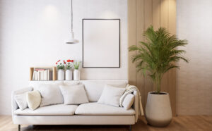 Modernes Wohnzimmer mit einem weißen Sofa voller weißer Kissen, einem Regal mit Büchern und Blumenvasen, einer großen grünen Zimmerpflanze und einer weißen Hängelampe.