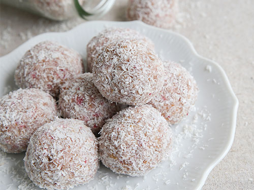 Hausgemachter Bliss Ball mit Erdbeeren, Datteln, Cashewkernen und Kokosnuss auf Vintage-Geschirr.