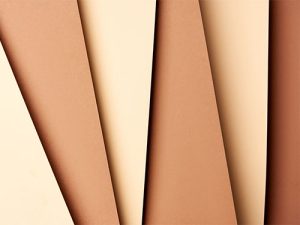 Mehrere Papierbögen in verschiedenen Beige- und Brauntönen liegen überlappend und diagonal angeordnet