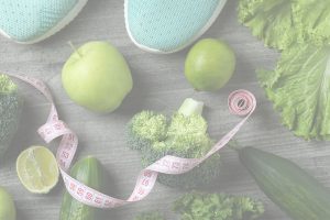 Eine Auswahl frischer grüner Lebensmittel und Fitnessartikel liegt auf einer grauen Holzoberfläche.